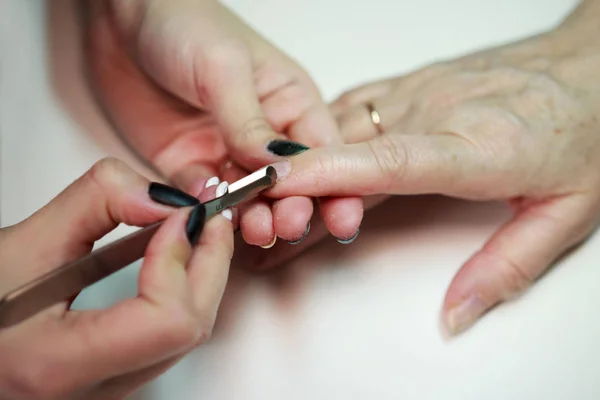 Manicurista servicio de uñas hace una mujer mayor con una herramienta de metal - una lanceta con una espátula en el extremo. Saliendo de la cutícula de las uñas. reportar disparos . — Foto de Stock