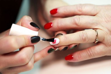 Üstat, kırmızı ve beyaz bir manikürdeki tırnaklarına gül yapıştırıyor. Ateş edildiğini bildiriyor.