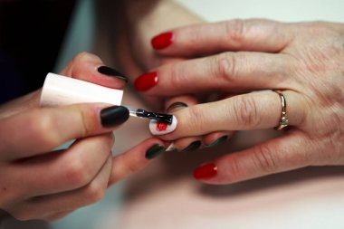 Üstat, kırmızı ve beyaz bir manikürdeki tırnaklarına gül yapıştırıyor. Ateş edildiğini bildiriyor.