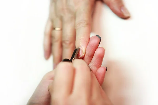 Manicurista servicio de uñas hace una mujer mayor con una herramienta de metal - una lanceta con una espátula en el extremo. Saliendo de la cutícula de las uñas. reportar disparos . — Foto de Stock