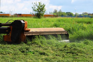 Kentsel çimlerde çim biçen bir traktörün başlığı. Traktör çimleri özel bir çim biçme makinesiyle biçiyor dairesel bıçaklarla..