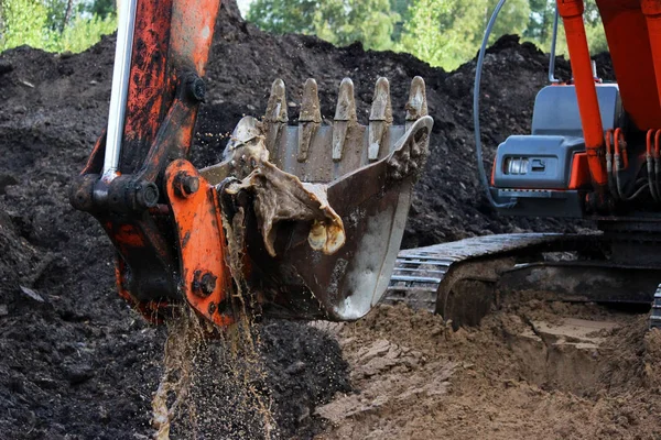 Bagr čerpá vodu z příkopu pomocí kbelíku, kterým projede cesta. období dešťů. opravy a rozšíření silnice. kruhy z betonu. Gatčína, Rusko, reportáž. — Stock fotografie