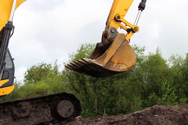 La excavadora del cubo sobre el fondo del follaje verde del árbol y el cielo azul. Extensión de reparación de carreteras en Gatchina, Rusia. reportaje . — Foto de Stock