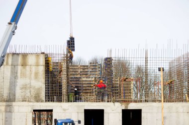 İşçi ve vinç operatörü, betondan güçlendirilmiş ve biçimlendirilmiş modern teknolojiyle büyük bir sağlık merkezi inşa etmek için güçlendirilmiş beton duvarlarla dolu arabayı boşaltıyor.