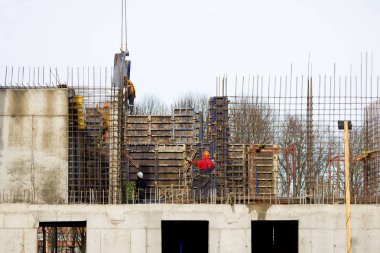 İşçi ve vinç operatörü, betondan güçlendirilmiş ve biçimlendirilmiş modern teknolojiyle büyük bir sağlık merkezi inşa etmek için güçlendirilmiş beton duvarlarla dolu arabayı boşaltıyor.