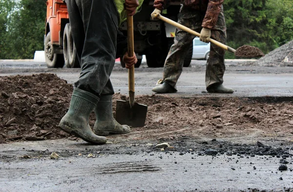 Pracovníci s lopatami připravují část cesty pro asfaltování pomocí záplatové metody. opravy a rozšíření silnice. Gatčína, reportáž. — Stock fotografie