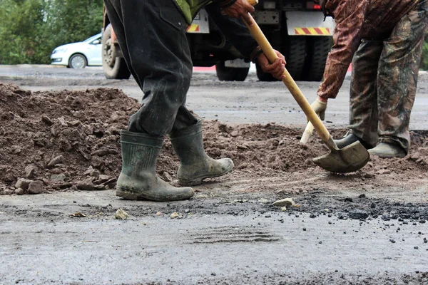 Los trabajadores con palas preparan parte de la carretera para asfaltar utilizando el método de parche. reparación y ampliación de la carretera. Gatchina, reportaje . — Foto de Stock