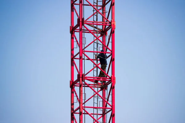 O operador do guindaste sobe as escadas para um grande guindaste vermelho para a construção de um grande centro de saúde na cidade de Gatchina. Contra o céu. Reportagem . — Fotografia de Stock