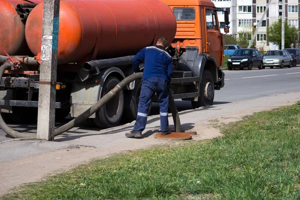 İşçi gece adamı kanalizasyon sisteminden sokaktaki kapaktan atık su pompaladı. Sokak temizleme borusunda kanalizasyon işçisi.