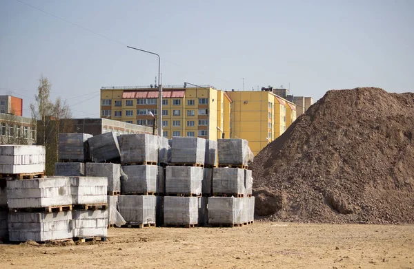 Molti cordoli per lavori di costruzione su pallet e una montagna di sabbia presso il sito posa lastre di pavimentazione piazza della città. reportage . — Foto Stock