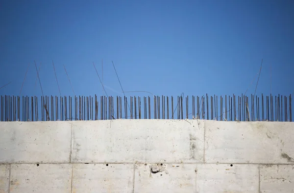 Ściana budynku, zbudowana z płyt i końców drutu zbrojeniowego na błękitnym niebie. — Zdjęcie stockowe