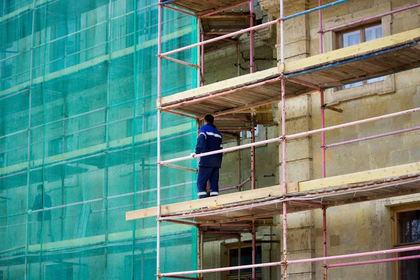 Restauratie van het Gatchina paleis. werknemer staat op steigers. een deel van het paleis is bedekt met een beschermend groen rooster. reportage. — Stockfoto