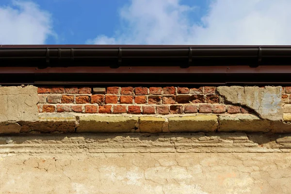 Tijolo bege velho parede rebocada uniformemente iluminado pelo sol. fundo texturizado industrial. com um fragmento que caiu da velhice — Fotografia de Stock