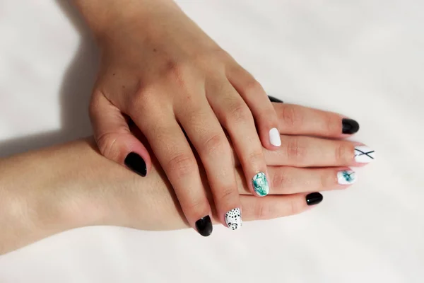 Handen van een jong meisje met groene, zwarte en witte manicure, met stickers. — Stockfoto