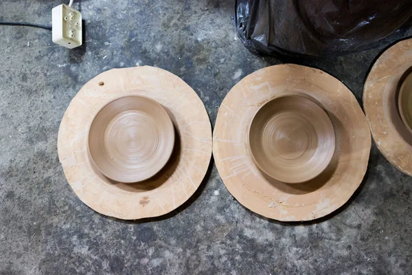 Ein Keramikmeister mit 13 Jahren Erfahrung fertigte mehrere Platten aus rotem Ton auf einer Töpferscheibe, auf einer Spanplatte zur besseren Entfernung und weiteren Trocknung. Reportagen — Stockfoto