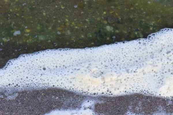 Sea foam and green water in the sea lagoon. the lagoon is a bay separated from the sea. the color of water is due to special microflora — Stock Photo, Image