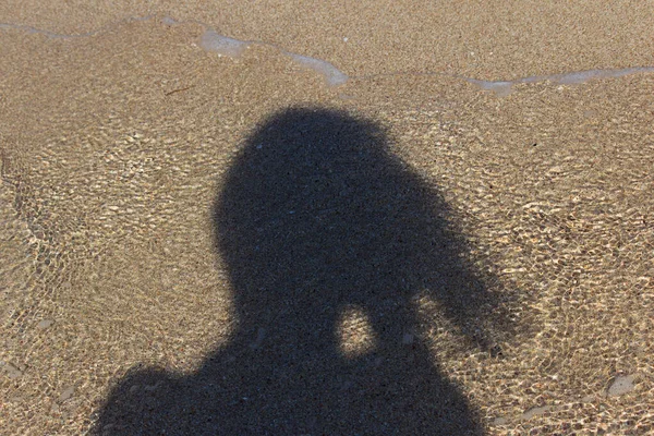 Sombra de una chica en el fondo de la ola de mar que se aproxima. Playa arenosa — Foto de Stock