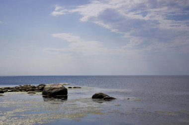 Körfezdeki gümüş mavisi su. Güneş, suyun yüzeyine yansıyor. Derin değil, suda büyük taşlar var. Gemiler için tehlike