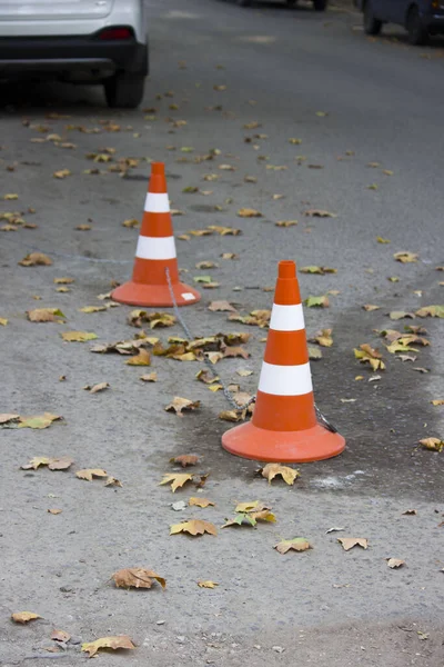 Restricciones en un estacionamiento vacío. Limitadores de carretera anaranjados y blancos conectados por una cadena custodian el espacio de estacionamiento en la carretera. — Foto de Stock