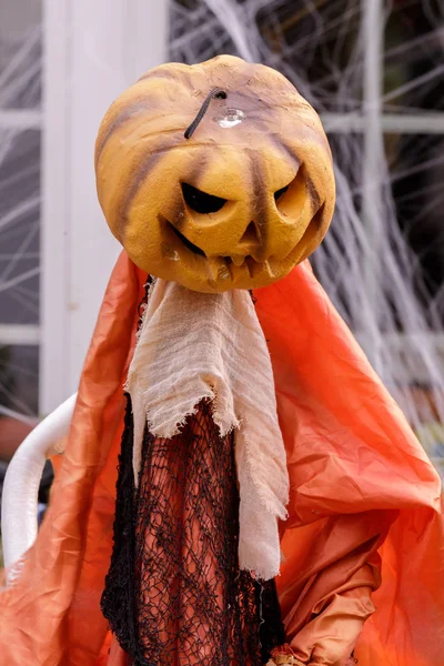 Pumpkin head scarecrow decorating home exterior in Halloween season. Spooky Halloween scarecrow with pumpkin head outside residential building.