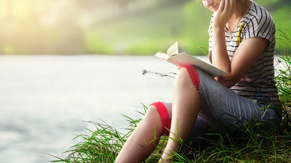 beautiful woman reading a book in the nature.brunette in a striped T-shirt reading a book against the background of a river