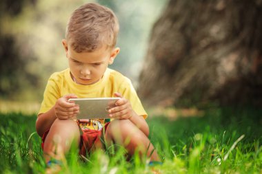 Küçük bir çocuk grass.little çocuk sarı bir tişört ve kırmızı şort bir akıllı telefon ile çimlerde oturan telefonda oturuyor