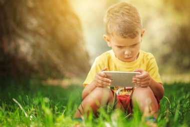 Küçük bir çocuk grass.little çocuk sarı bir tişört ve kırmızı şort bir akıllı telefon ile çimlerde oturan telefonda oturuyor