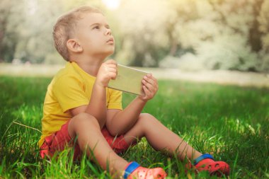 Küçük bir çocuk grass.little çocuk sarı bir tişört ve kırmızı şort bir akıllı telefon ile çimlerde oturan telefonda oturuyor