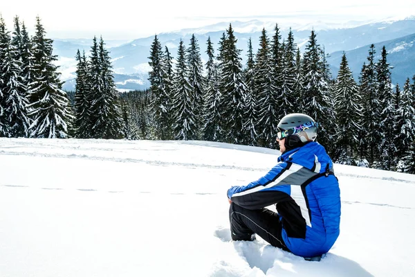 Bir dağın tepesinde kar kış spor giyim seyir uzakta, giyen büyük yansıtılmış Kayak mask.a adam mavi Kayak takım elbiseli Genç yakışıklı adam oturuyor