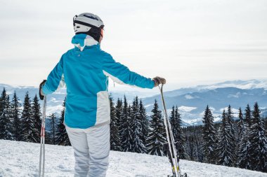 mavi bir takım elbise, kask ve gözlük bir kadında kayaklar bir dağın tepesinde ile ayakta.
