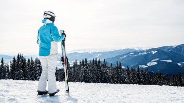 mavi bir takım elbise, kask ve gözlük bir kadında kayaklar bir dağın tepesinde ile ayakta.