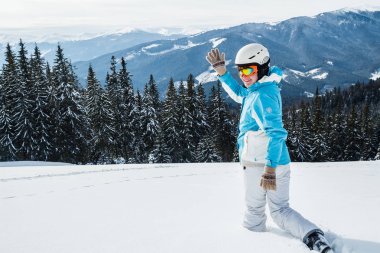 Karda dağ üstündeki beyaz ve mavi elbiseli kadın kayakçı.
