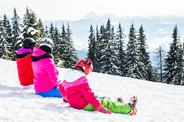 Bir grup insan kırmızı Kayak takım elbiseli bir dağın tepesinde kar üzerinde oturuyor. Bir aile kayakçı kar üzerinde oturmuş dinleniyor