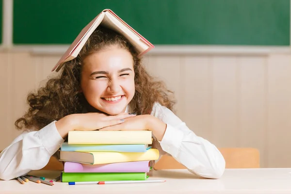 緑色の板の背景に本と鉛筆を持つ彼女の机に座って制服の女子高生 女の子が本と彼女の頭をカバー — ストック写真