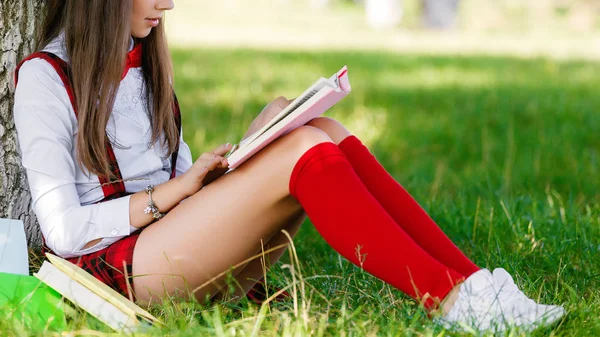 Молода школярка в шкільній формі сидить на траві під деревом з книгами — стокове фото