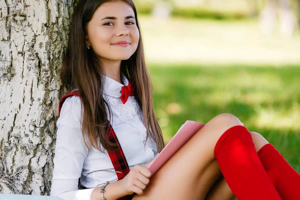 젊은 여 학생 학교 유니폼 책 나무 아래 잔디에 앉아 — 스톡 사진