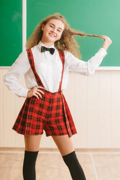 Bela jovem estudante em uniforme escolar de pé no fundo da diretoria da escola — Fotografia de Stock