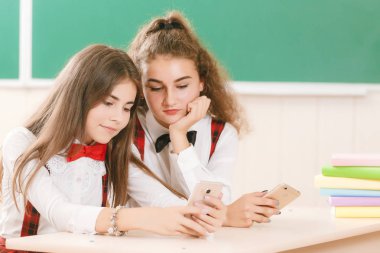 kız öğrenciler okul üniformalı çiftler sınıfta oturmak. Kızlar okula gidiyorum. Kız öğrenciler sınıfta kitap okumak ve bir akıllı telefon kullanma
