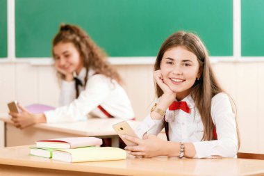 kız öğrenciler okul üniformalı çiftler sınıfta oturmak. Kızlar okula gidiyorum. Kız öğrenciler sınıfta kitap okumak ve bir akıllı telefon kullanma