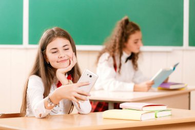 kız öğrenciler okul üniformalı çiftler sınıfta oturmak. Kızlar okula gidiyorum. Kız öğrenciler sınıfta kitap okumak ve bir akıllı telefon kullanma