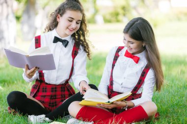 İki komik liseli kız çimlerin üzerinde oturup kitap okuyor. Kızlara, kız arkadaşlara, kız kardeşlere doğa dersleri verilir..