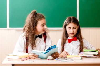 iki brun.ette kız öğrenciler tahtanın arka planda kitaplar ile masasında sınıfta oturup.kızlar bir okul dersi oturup