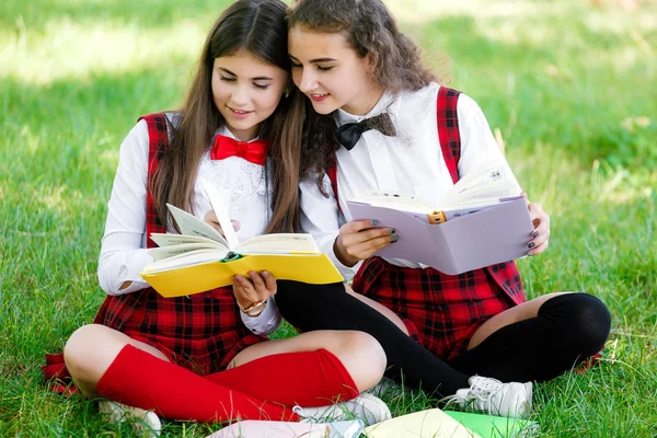 赤い制服を着た女子中学生が Books Girlfriends と緑の芝生の上に座る または姉妹屋外授業 — ストック写真