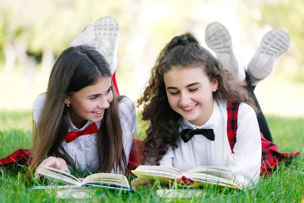 Дві Школярки Червоній Шкільній Формі Лежать Зеленому Газоні Книгами — стокове фото
