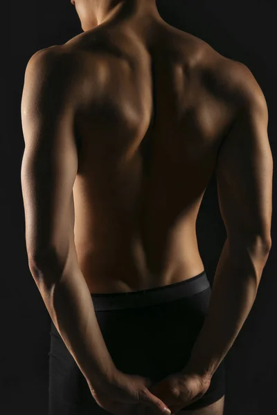 Beautiful sporty men\'s back and hands clasped into the lock behind the back. Male athletic body close-up on black background back view
