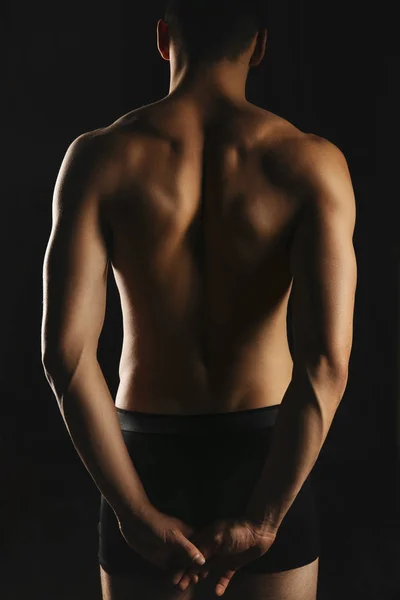 Beautiful sporty men\'s back and hands clasped into the lock behind the back. Male athletic body close-up on black background back view