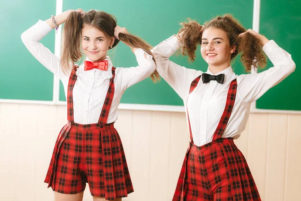 교 복에 두 예쁜 여 학생 교실 칠판의 배경에서 서와 서 — 스톡 사진