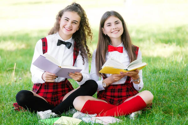 two schoolgirls in school uniforms sit with books in the park. Schoolgirls or students are taught lessons in nature