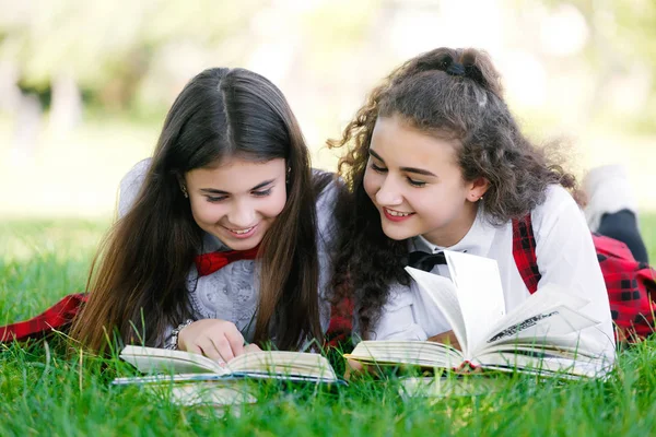 two schoolgirls in school uniforms sit with books in the park. Schoolgirls or students are taught lessons in nature