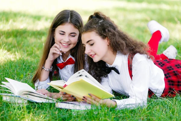 Дві школярки в шкільній формі сидять з книгами в парку. Школярки або студенти викладають уроки на природі — стокове фото